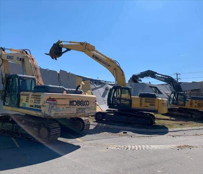 Three large yellow Excavators are shown taking down a damaged commerical building.