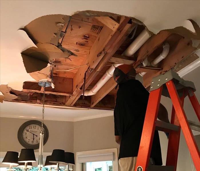 Servpro employee on oranger ladder, removing wet drywall from kitchen ceiling.