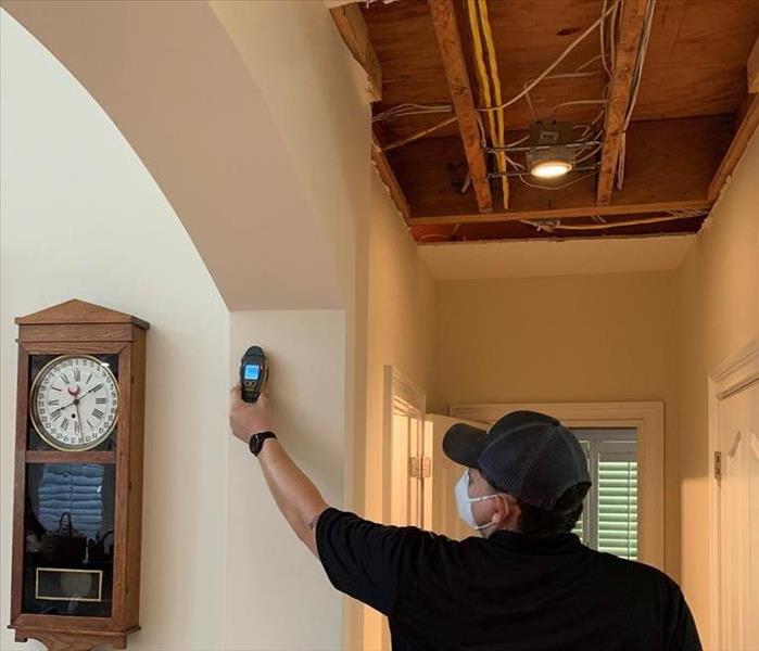 SERVPRO team member in black polo and SERVPRO hat checks for moisture using a moisture meter. 