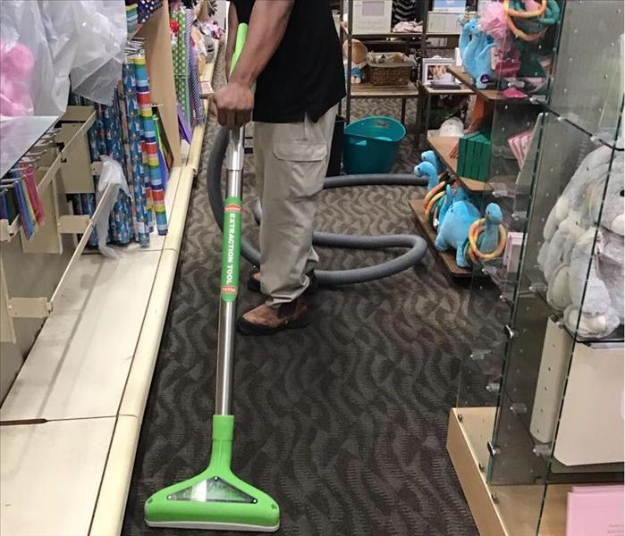 Servpro employee with using green extractor wand to remove remainging water out of carpet.