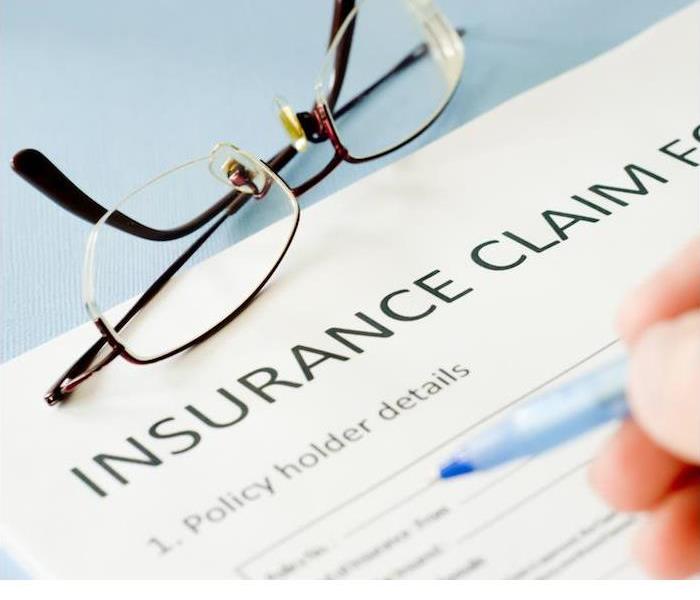 insurance claim document and reading glasses sitting on blue desk