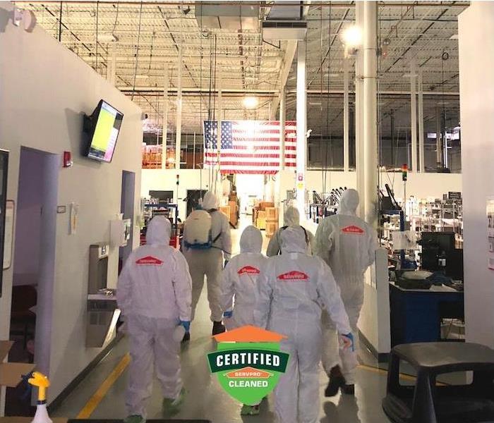 a group of SERVPRO workers in PPE gear walking inside commercial factory