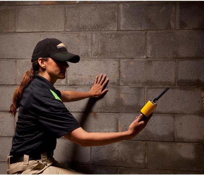 A woman who works for SERVPRO checking for moisture in a basement with a moisture meter