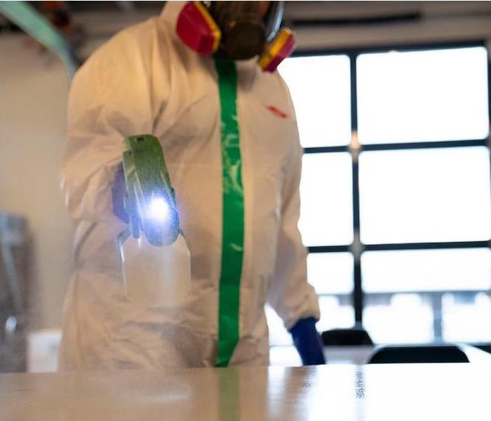 a SERVPRO employee in PPE gear spraying cleaner